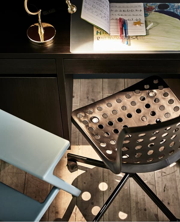 A desk chair with circular cut-outs for a child and a stool for a parent to do homework together, sitting at the desk.