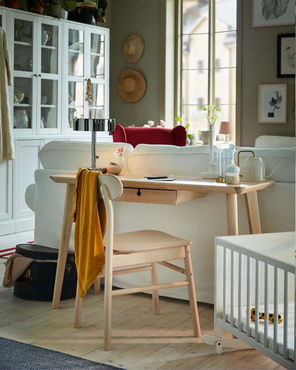 A desk in ash veneer is standing behind an EKTORP sofa, and the desk provides a workspace in a living room.