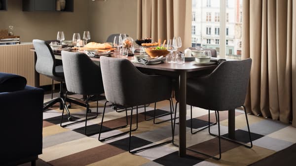 A dining area by a window with a large dining table, six metal black/grey TOSSBERG chairs and two dark grey office chairs.