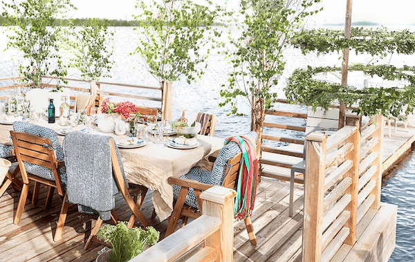 A dining area set for a party sits on a dock in a lake.