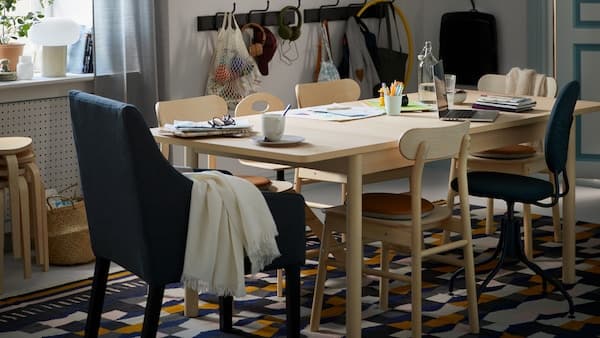 A dining area with a RÖNNINGE birch table with various items placed on it, and RÖNNINGE chairs on a TÅRBÄK rug.