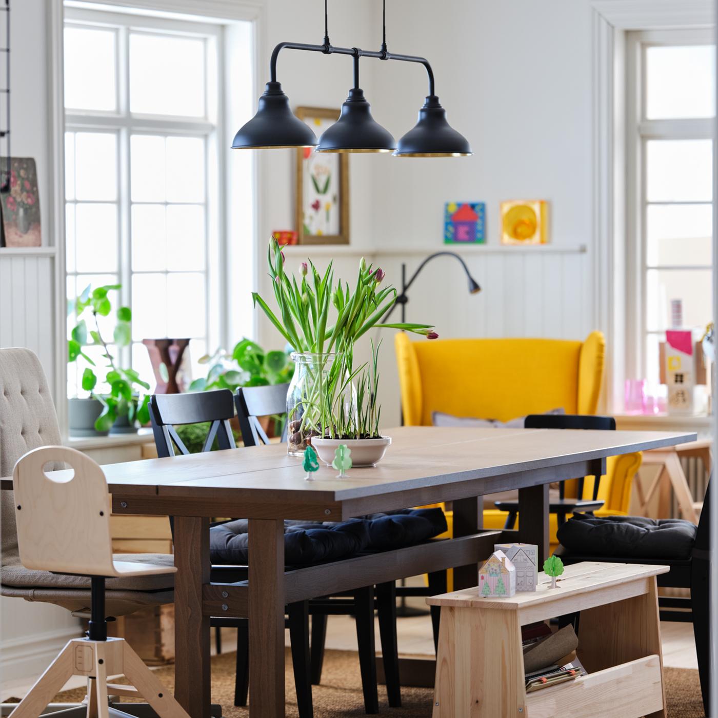 A dining area with a table, chairs and lamps in a large, light and airy room.
