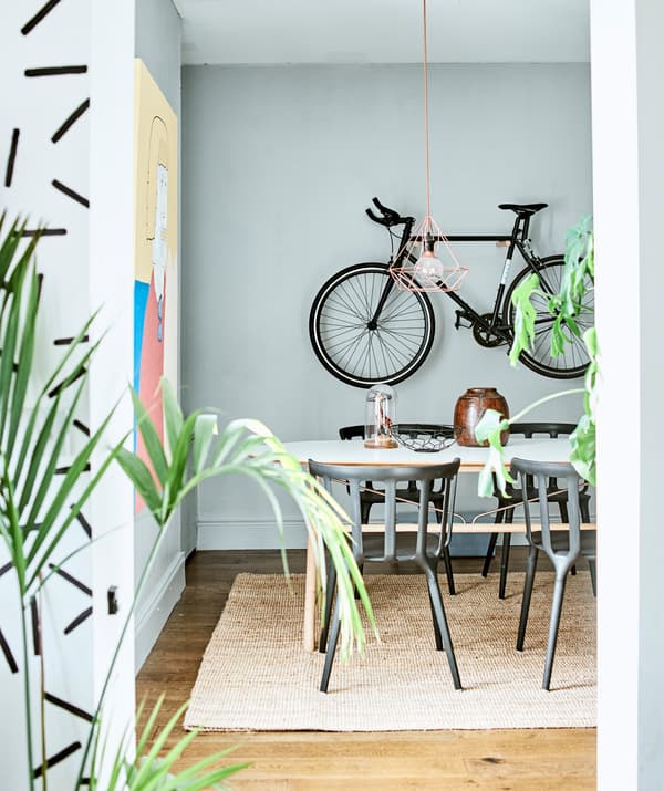 A dining area with table and chairs, plants and a bike hanging on the wall.