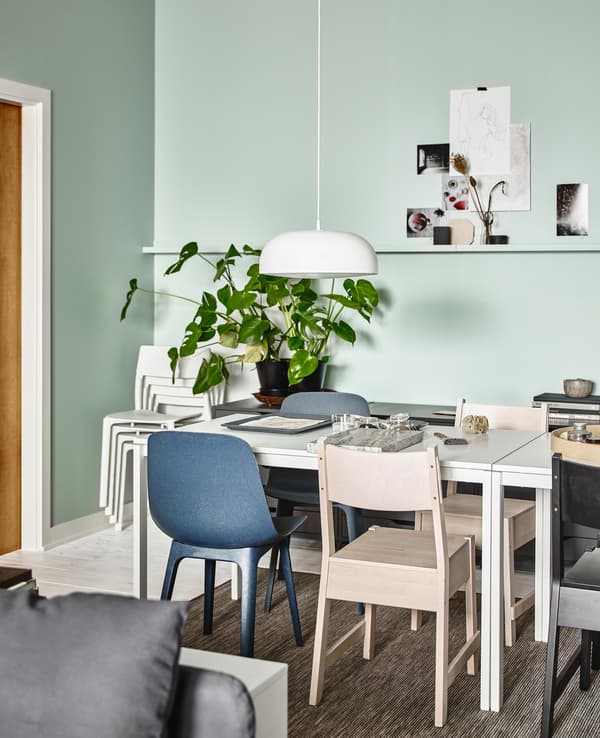 A dining room area in an open living space, with MELLTORP white dining tables surrounded by a mix of different styled chairs.