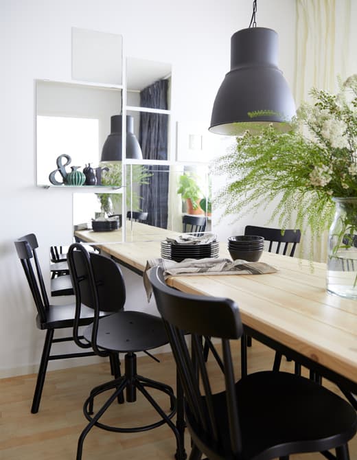A dining room wall is decorated with several rectangular and square mirrors above a dining table.