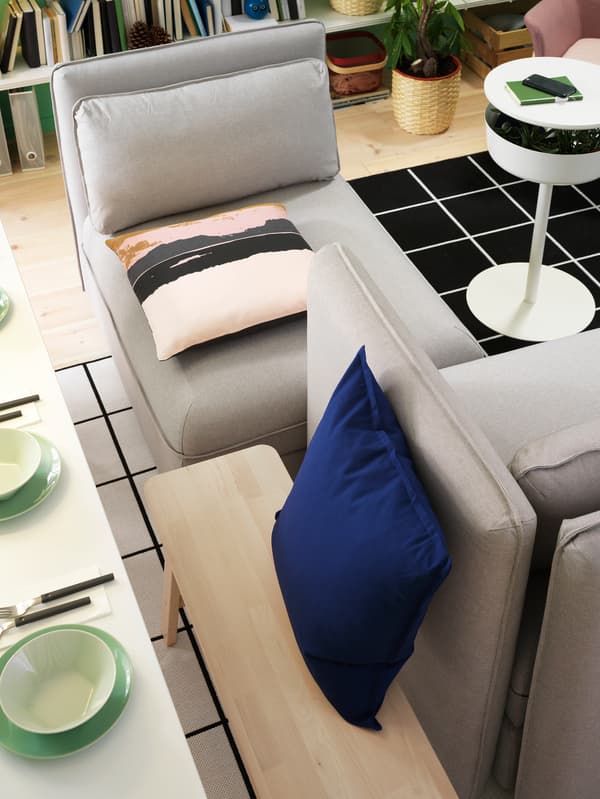A dining room with a table, a bench and a grey sofa. The backside of the backrest is used as a backrest for the bench.