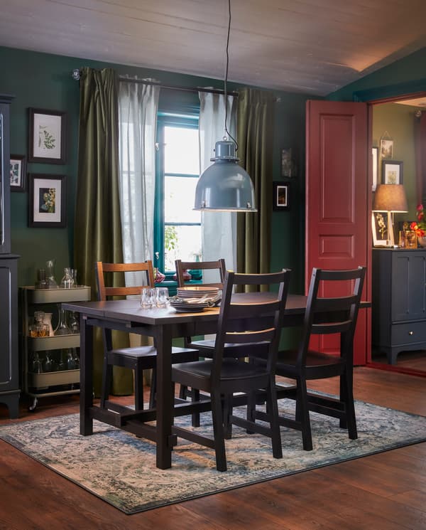 A dining room with a table and four chairs in black, an oriental-patterned rug and a grey-turquoise pendant lamp.