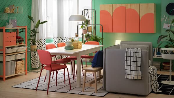 A dining room with a white table, red chairs, and gray sofa and a cabinet and a shelving unit painted in coral color.