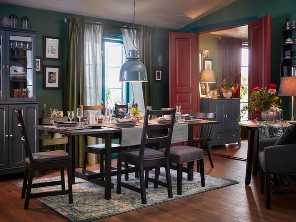 A dining room with an extended table and five chairs in black, an oriental-patterned rug and a grey-turquoise pendant lamp.