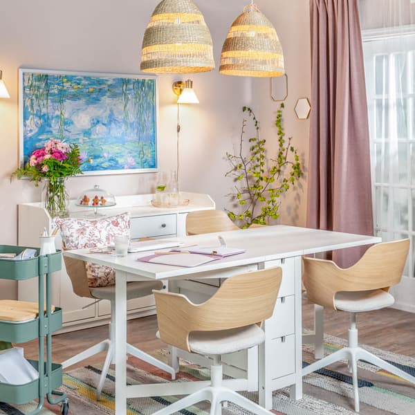 A dining space turned into a home office. In the middle of the room is a dining table used as a work desk along with four chairs. Beside the table, a cart with casters holds office supplies and a storage basket.