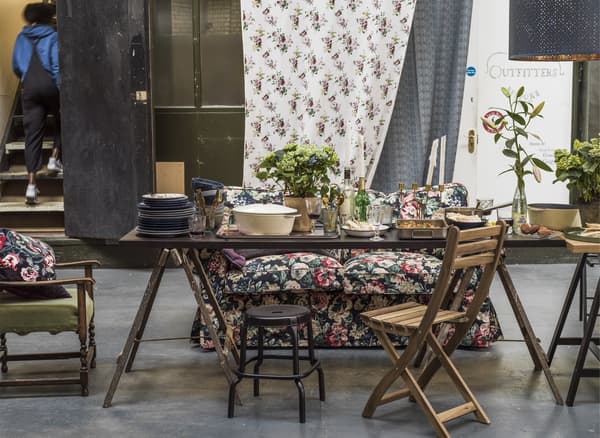 A dining space with mismatched chairs, potted plants and a floral sofa.