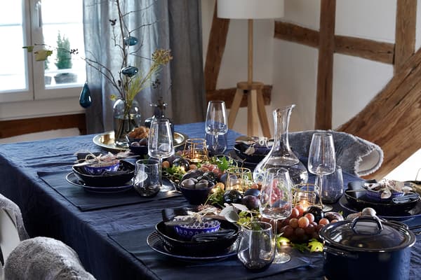 A dining table decorated with a blue tablecloth, blue place mats, and an elegant mix of different plates. 