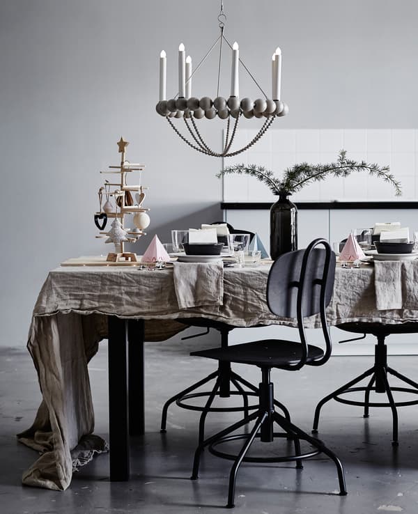 A dining table decorated with pastel origami, greenery in a vase and a wooden board down the center of the table.