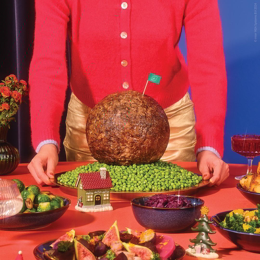 A dining table filled with various vegetables and meats for dinner, a giant meatball in the middle