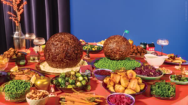 A dining table filled with various vegetables and meats for dinner, including two giant meatballs in the middle