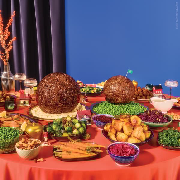 A dining table filled with various vegetables and meats for dinner, including two giant meatballs in the middle