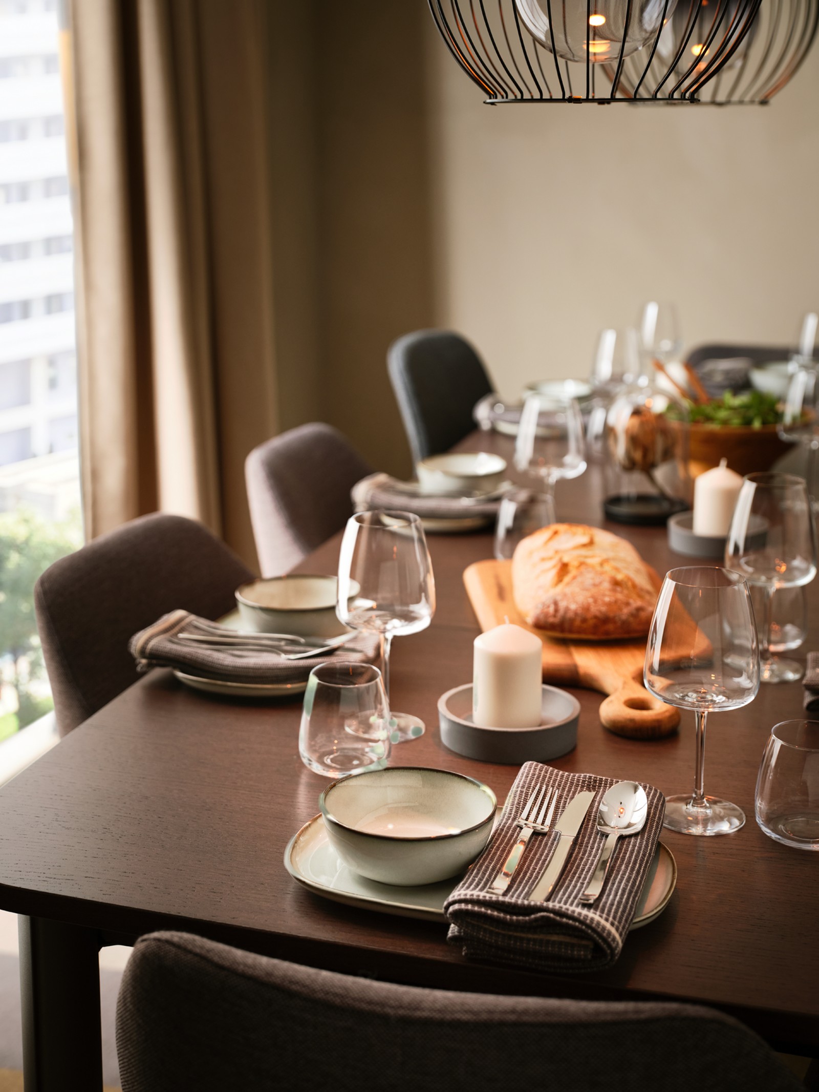 A dining table laid with GLADELIG plates and bowls, with a chopping board in the middle of the table holding a loaf of bread.