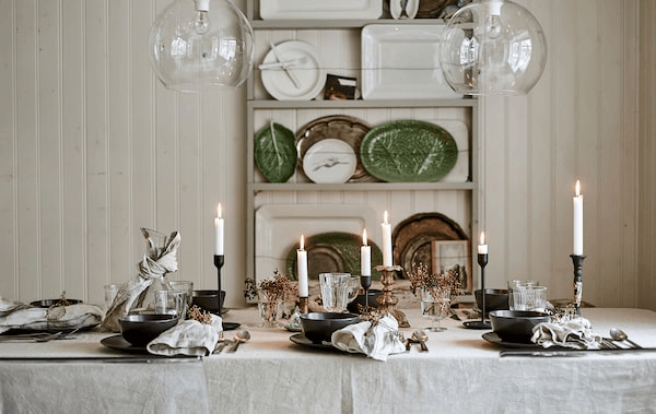 A dining table set for a festive meal with linen table cloth, candles, glassware and place settings with decorated napkins.