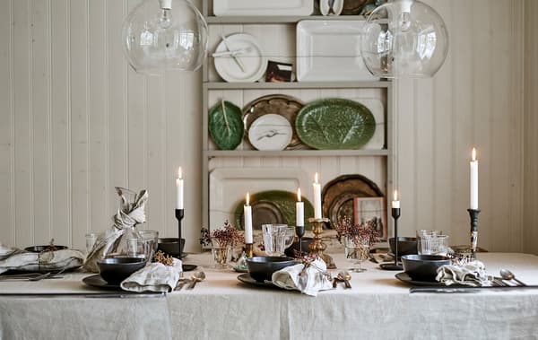A dining table set for a festive meal with linen table cloth, candles, glassware and place settings with decorated napkins.