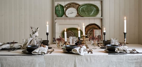 A dining table set for a festive meal with linen table cloth, candles, glassware and place settings with decorated napkins.