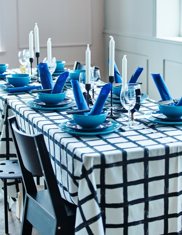 A dining table with a chequered black and white table cloth decorated with blue plates, bowls, napkins and candles.