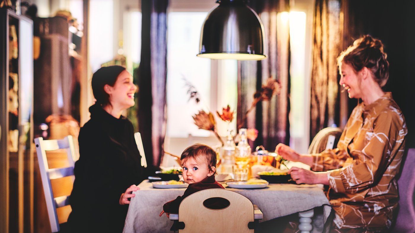 A dining table with a pendant lamp. A toddler, mom and grandmother sitting around the table while eating and laughing.