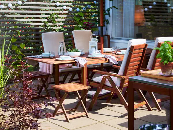 A dining table with drop-leaves, 4 reclining chairs and 2 foldable stools in acacia. White dinnerware stands on the table.