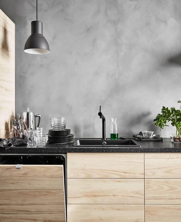 A dishwasher with integrated ash effect panels in a row of base cabinets in a modern rustic kitchen with grey, concrete-looking walls 