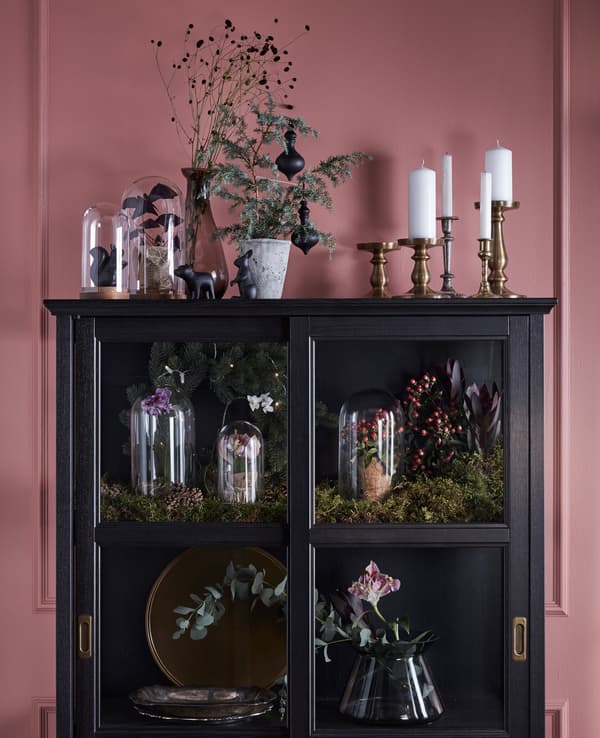 A display cabinet is decorated and filled with greenery, flowers and glass domes.