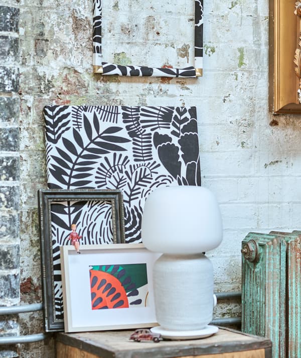 A display of patterned fabrics framed in different ways, set against a brick wall, on a tea crate with a white speaker light.