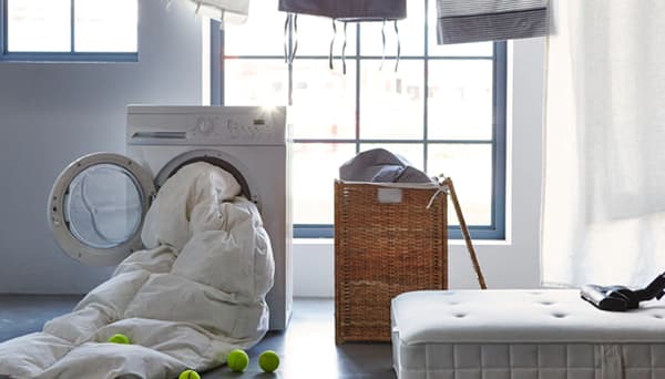 A display with an open laundry basket, a mattress with a vacuum on it and a tumble dryer with a quilt coming out 