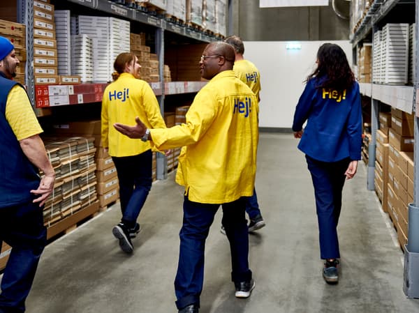 A diverse group of IKEA co-workers walk through the furniture self-service section of an IKEA store.