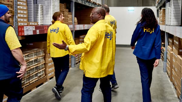 A diverse group of IKEA co-workers walk through the furniture self-service section of an IKEA store.