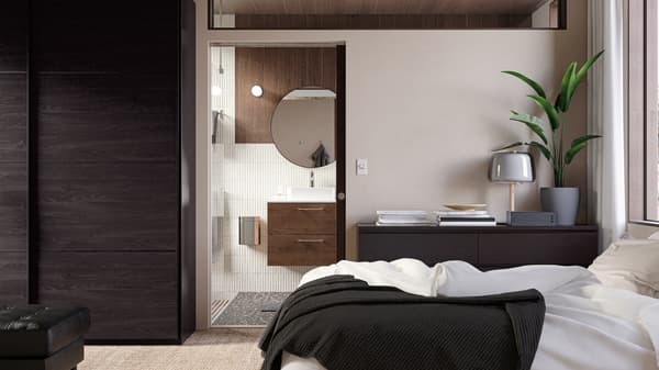 A door in the bedroom offers a peek into a stylish bathroom with a wooden washstand, a round mirror and beige tiles.