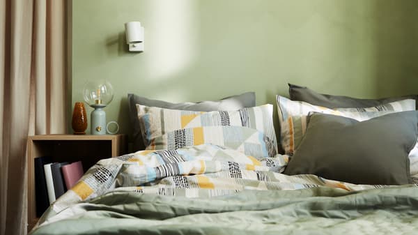 A double bed made with a duvet cover in an abstract pattern in green, yellow, black, beige and blue, and other green bedding.