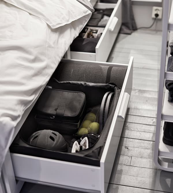 A drawer unit under the bed, slid open to show sports equipment kept tidy with interior organisers.