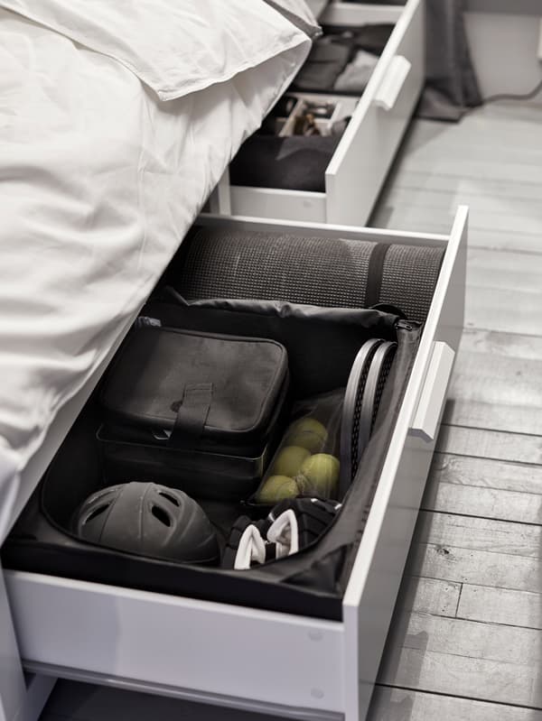 A drawer unit under the bed, slid open to show sports equipment kept tidy with interior organisers.