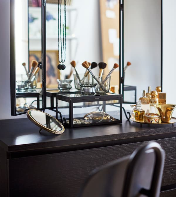 A dressing area with a wall mirror, a black chair, a tabletop and some make-up brushes.