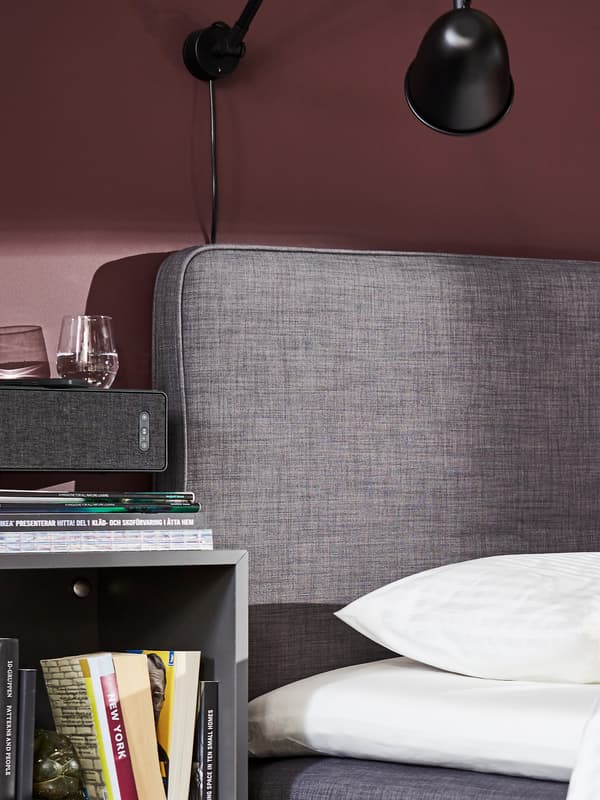 A DUNVIK divan bed in dark grey, white bed textiles and a black wall lamp.
