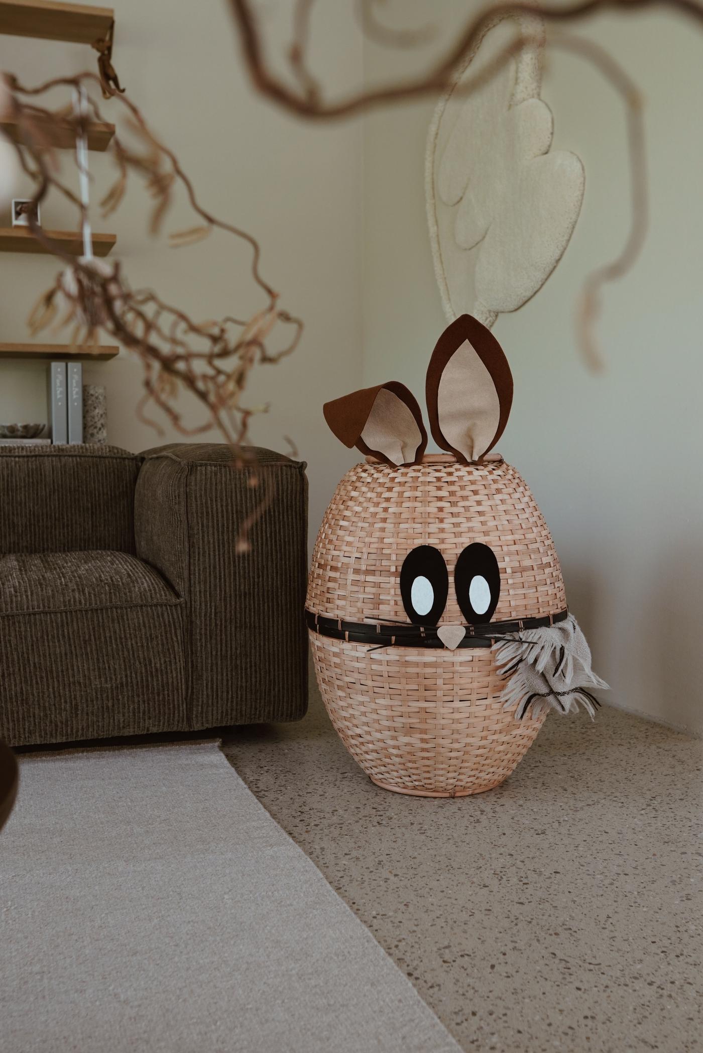 A easter bunny basket in the corner next to a couch.