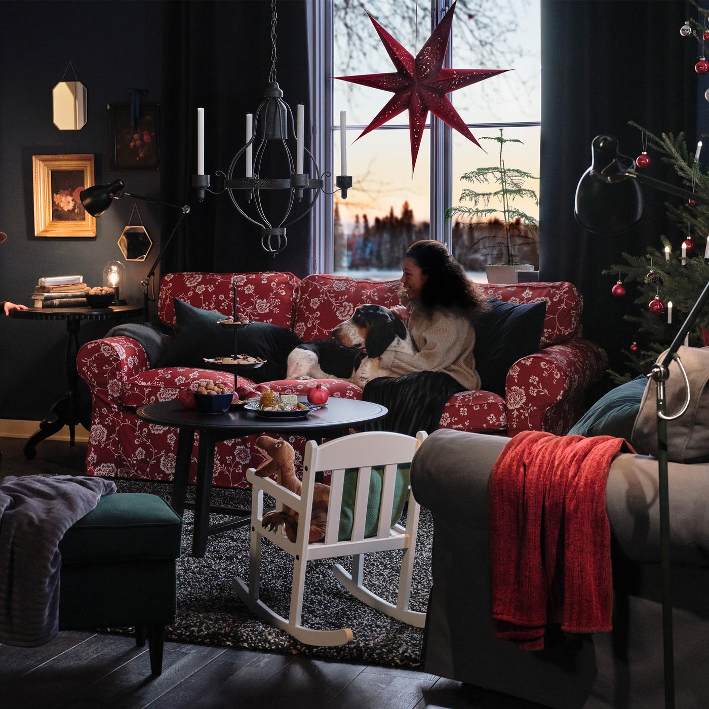 A family and their dog sit in their living room, waiting for a small girl, peeking through the door, to put on a show.