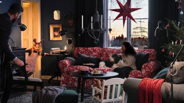 A family and their dog sit in their living room, waiting for a small girl, peeking through the door, to put on a show.