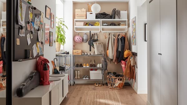 A family hallway with jackets hanging on white hooks and shelves, shoes on metal shelving units, a white storage bench.