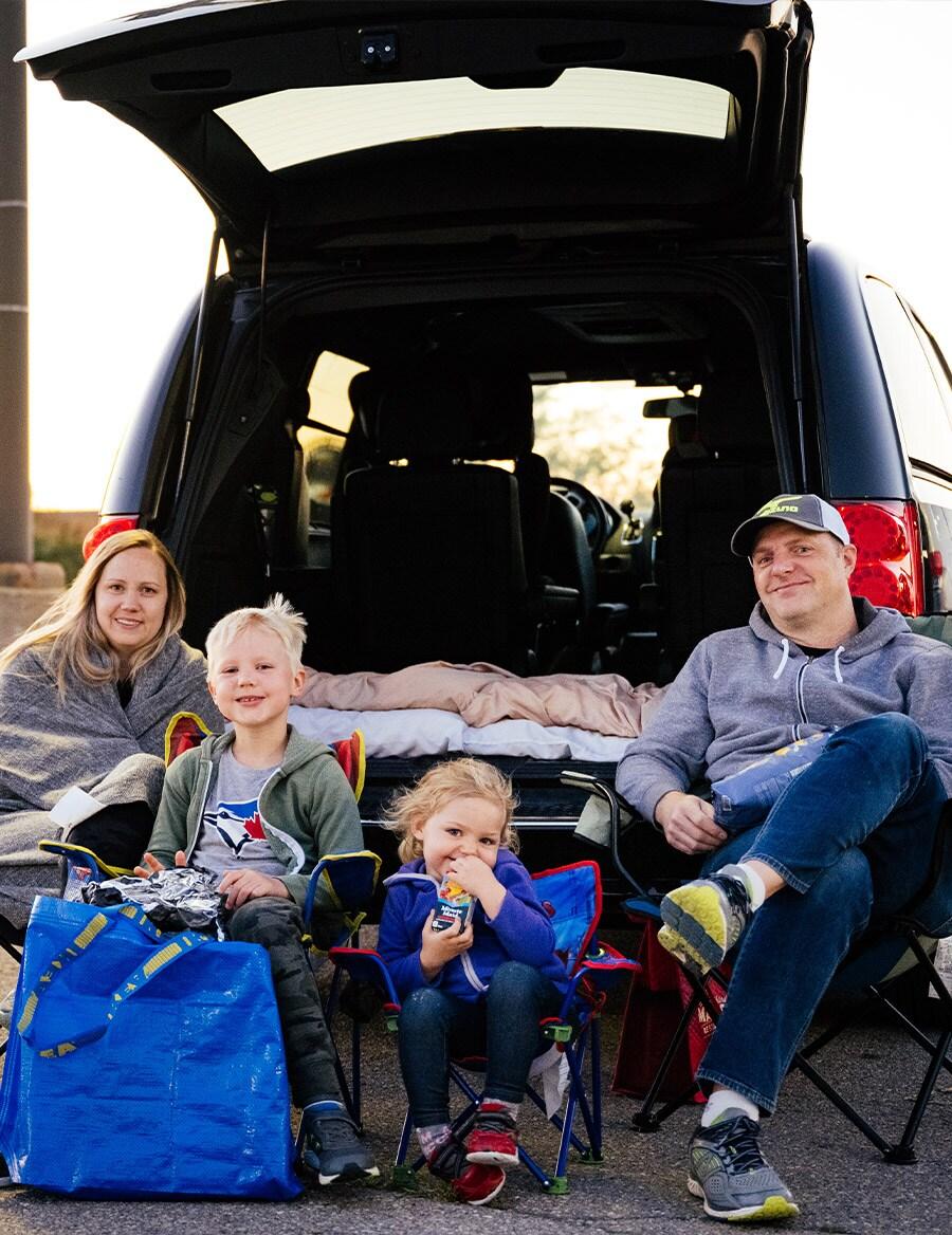 A family of four is sitting on camping chairs behind their SUV, getting ready to watch the drive-in movie.