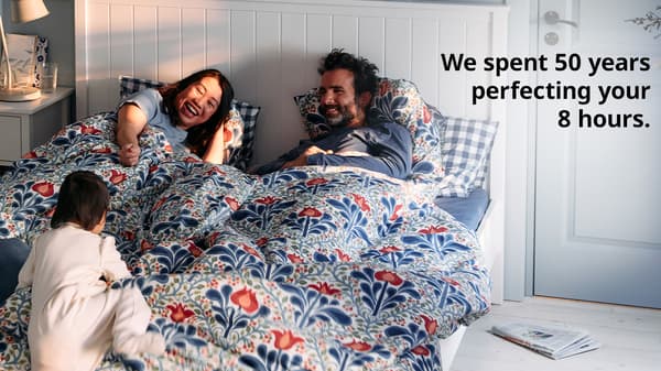 A family of three (asian mother, caucasian father) smiles at their daughter as she is climbing up a white GULLABERG bed frame in the bedroom.