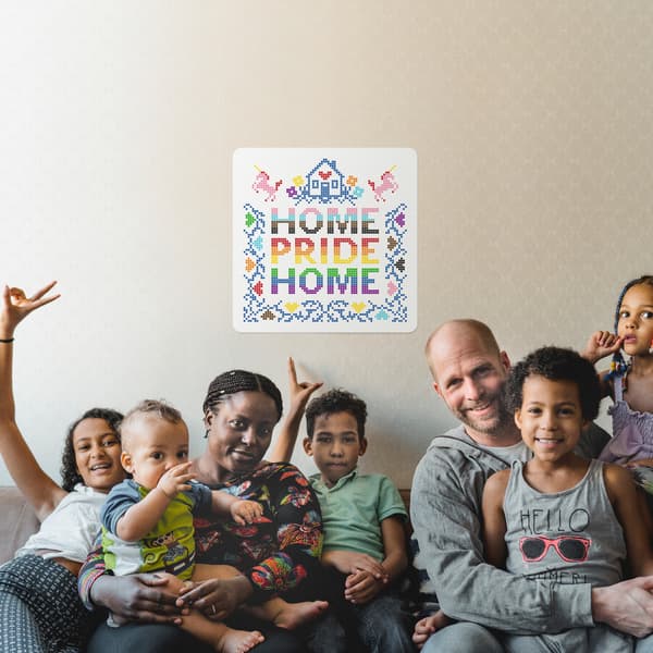 A family of two parents and five children sitting on a sofa with a Home Pride Home sign on the wall behind them.