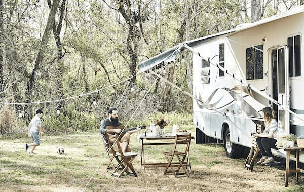 A family relaxing outside a motorhome in a rural setting.