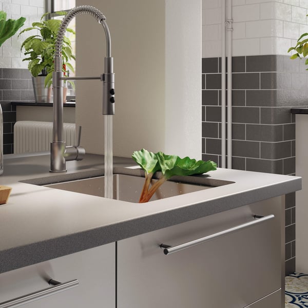 A faucet running watter into a stainless steel sink with a sleek quartz sink on a sink cabinet.