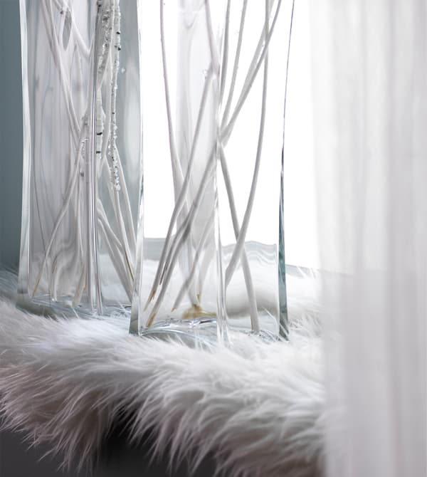 A faux sheep skin rug lines a window sill with glass vases filled with twigs.