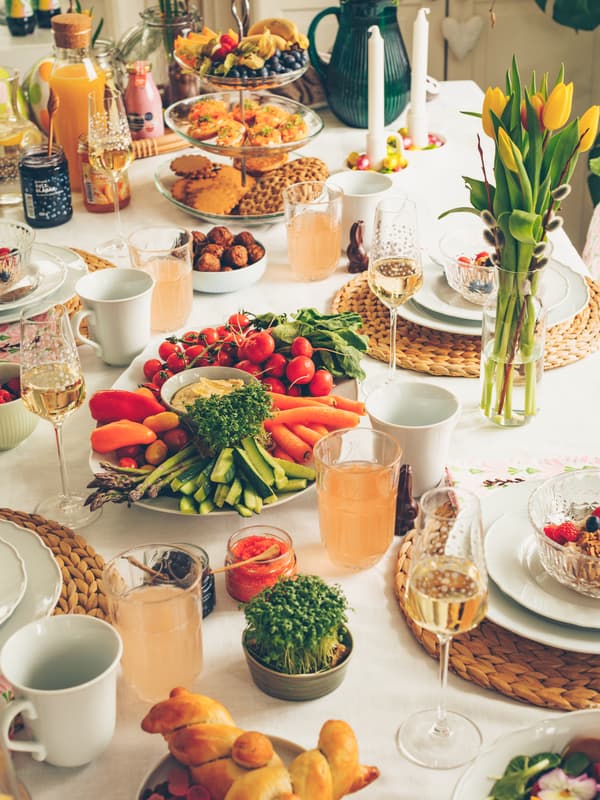 A festive table set with assorted fresh vegetables, dips, pastries, drinks, and elegant glassware for a meal gathering.